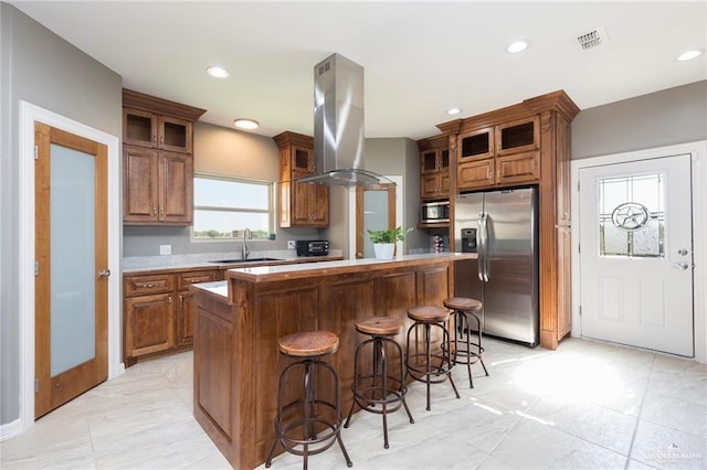 kitchen featuring appliances with stainless steel finishes, island range hood, sink, a kitchen island, and a breakfast bar area