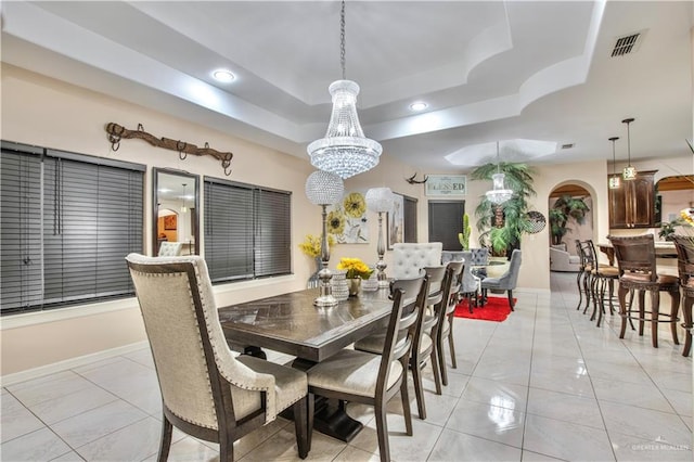 dining space with a raised ceiling, an inviting chandelier, and light tile patterned flooring