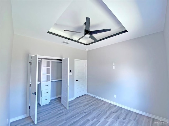 unfurnished bedroom featuring a raised ceiling, ceiling fan, a closet, and light wood-type flooring