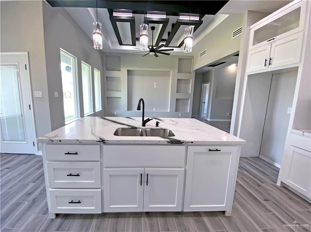 kitchen with light stone counters, sink, white cabinets, and pendant lighting