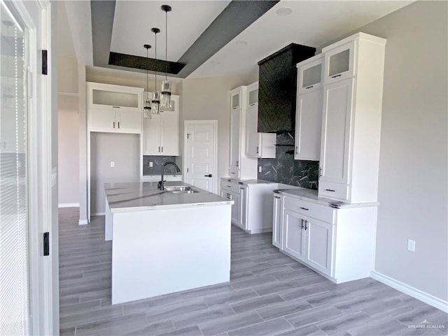 kitchen featuring white cabinetry, backsplash, a kitchen island with sink, and decorative light fixtures