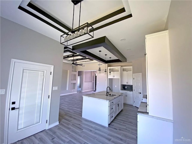 kitchen featuring white cabinetry, sink, pendant lighting, light hardwood / wood-style floors, and a kitchen island with sink