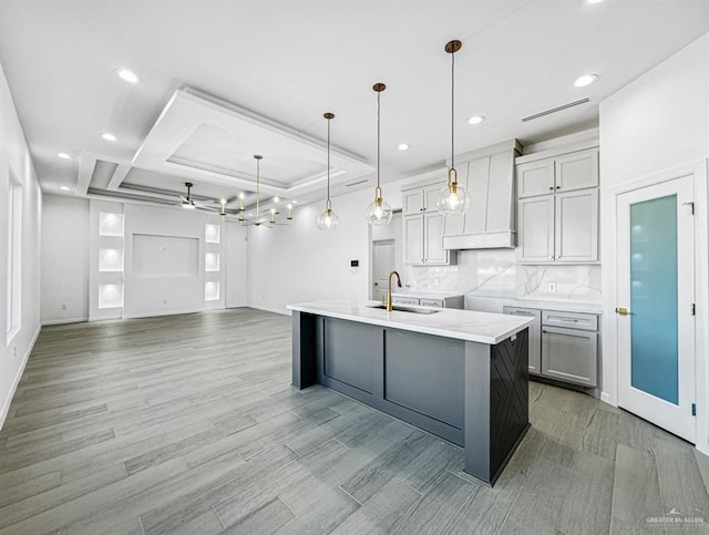 kitchen with decorative backsplash, light wood-style floors, premium range hood, pendant lighting, and a sink