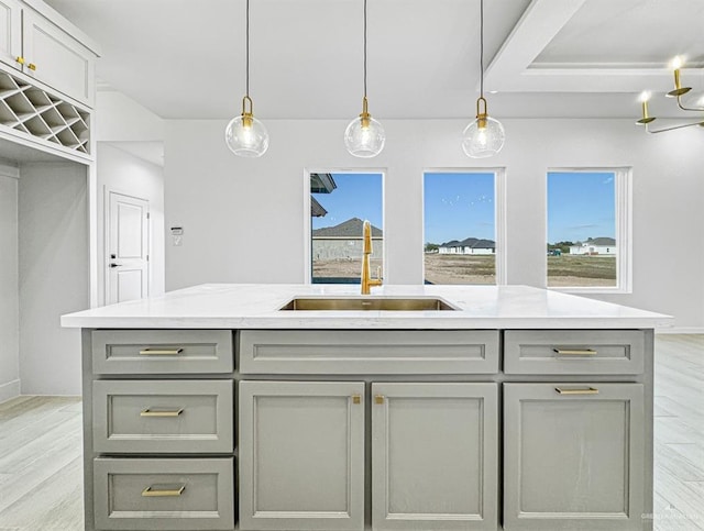 kitchen featuring light wood-style floors, a sink, hanging light fixtures, and gray cabinetry