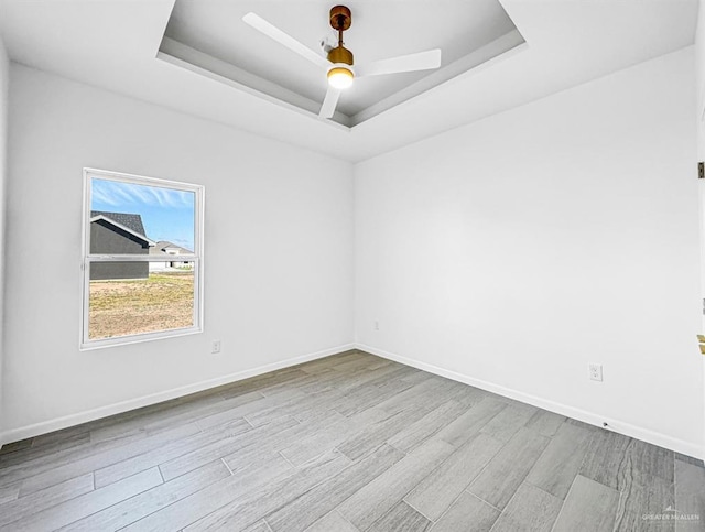 unfurnished room featuring baseboards, a raised ceiling, and wood finished floors