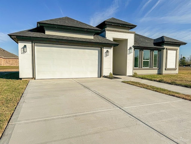 prairie-style home with a garage, concrete driveway, roof with shingles, a front yard, and stucco siding