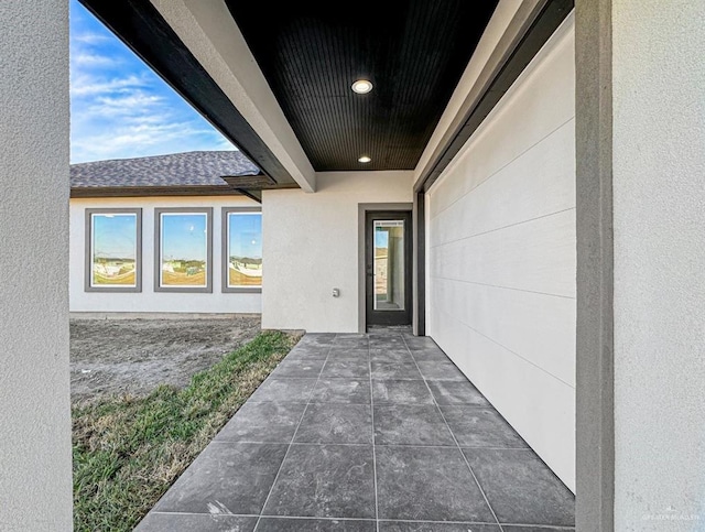 view of exterior entry featuring a patio, a shingled roof, and stucco siding