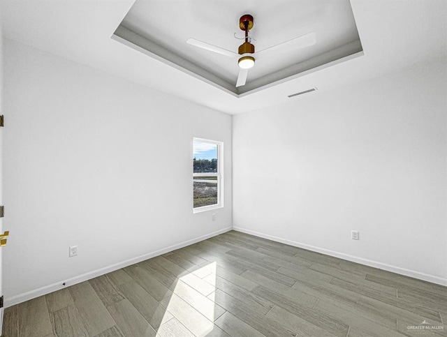 unfurnished room with baseboards, visible vents, ceiling fan, wood finished floors, and a tray ceiling