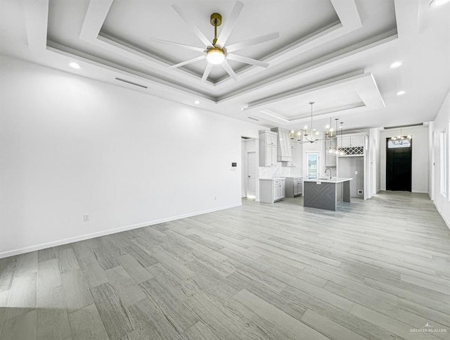 unfurnished living room with a tray ceiling, visible vents, light wood-style floors, a sink, and baseboards