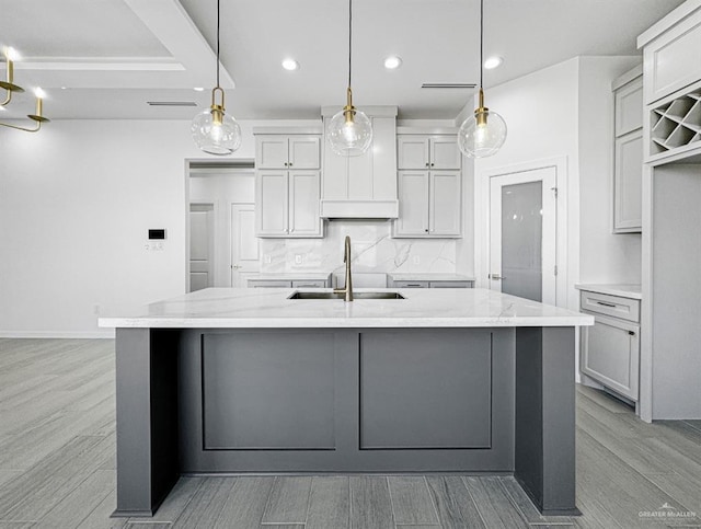 kitchen with a center island with sink, decorative backsplash, wood finish floors, a sink, and recessed lighting