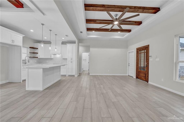 unfurnished living room with light wood-style flooring, coffered ceiling, a sink, baseboards, and beam ceiling