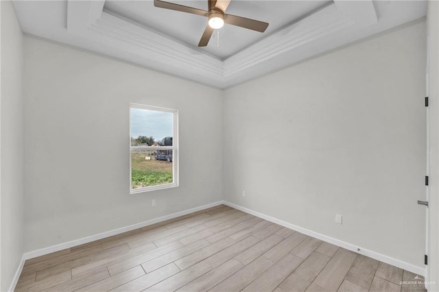 empty room featuring light wood-type flooring, a tray ceiling, ceiling fan, and baseboards