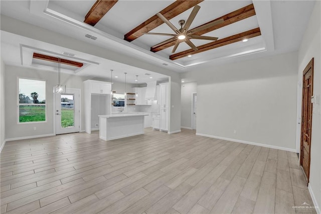 unfurnished living room featuring a tray ceiling, light wood-style floors, and baseboards