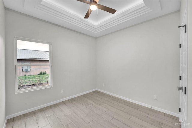 spare room featuring light wood finished floors, baseboards, a raised ceiling, ceiling fan, and ornamental molding