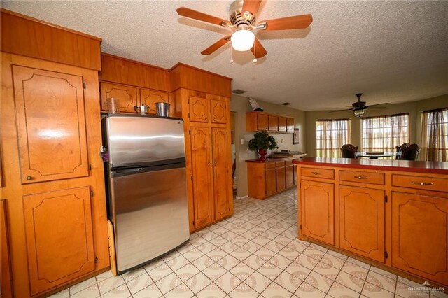 kitchen with a textured ceiling, brown cabinets, dark countertops, and freestanding refrigerator