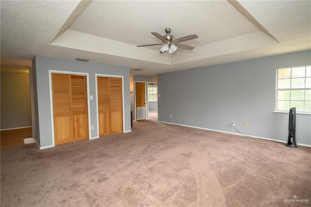 unfurnished bedroom featuring a textured ceiling, carpet, a tray ceiling, and multiple closets