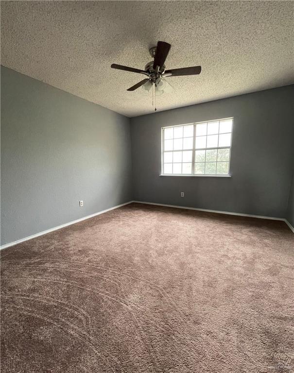 empty room with a ceiling fan, a tray ceiling, a textured ceiling, carpet flooring, and baseboards
