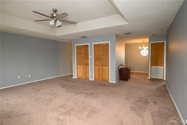 unfurnished bedroom featuring visible vents, two closets, baseboards, a textured ceiling, and a raised ceiling