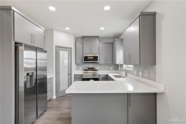 kitchen with stainless steel appliances, gray cabinetry, decorative backsplash, a sink, and a peninsula