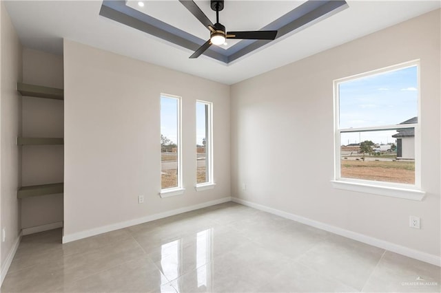 tiled spare room featuring ceiling fan and a tray ceiling