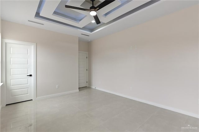 empty room with ceiling fan and a tray ceiling