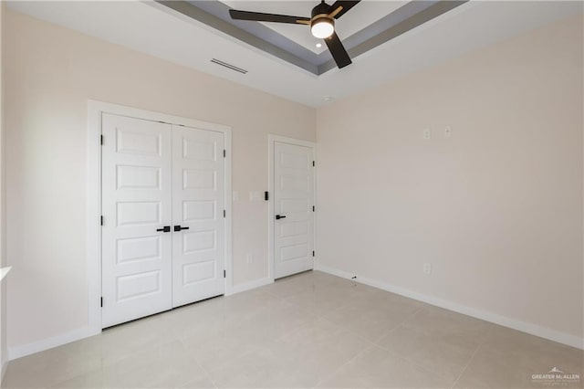 unfurnished bedroom featuring ceiling fan, a tray ceiling, and a closet