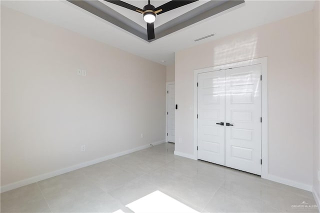 unfurnished bedroom featuring a closet, light tile patterned floors, a raised ceiling, and ceiling fan