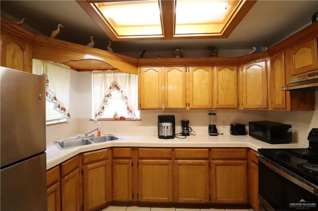 kitchen featuring brown cabinetry, a sink, under cabinet range hood, and black appliances