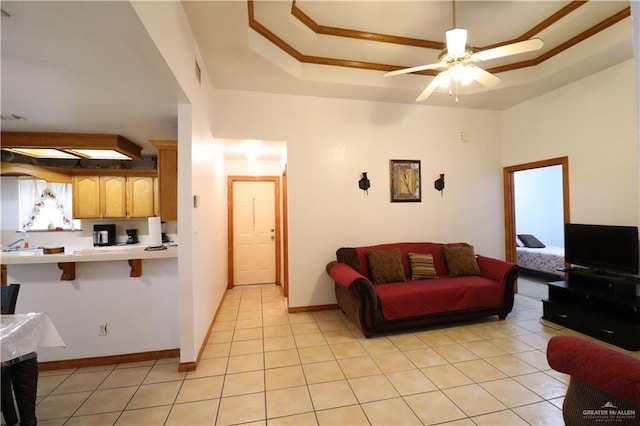 living area featuring light tile patterned floors, a raised ceiling, a ceiling fan, and baseboards