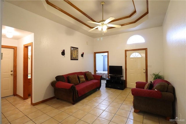 living area with a tray ceiling, light tile patterned flooring, ceiling fan, and baseboards