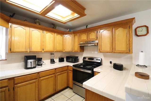 kitchen featuring electric stove, brown cabinetry, tile counters, and under cabinet range hood