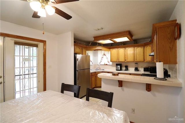 kitchen with tile countertops, a kitchen bar, freestanding refrigerator, and brown cabinets