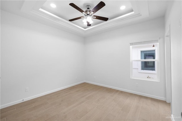 unfurnished room featuring ceiling fan, light wood-type flooring, a raised ceiling, and baseboards