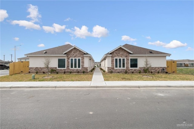 single story home featuring stone siding, a front yard, fence, and stucco siding