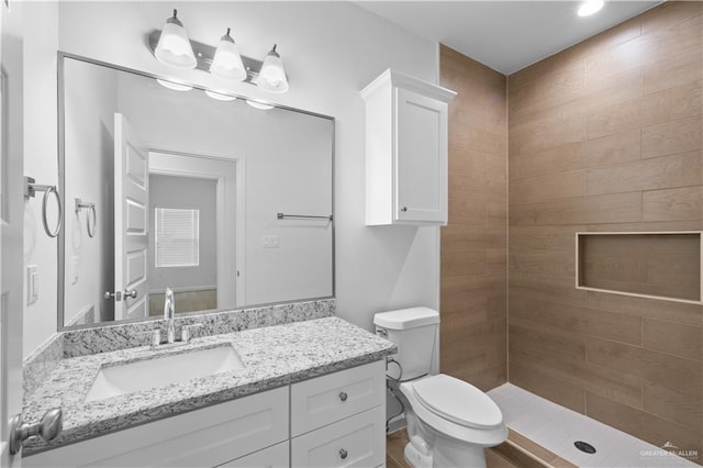 full bathroom featuring a tile shower, vanity, and toilet