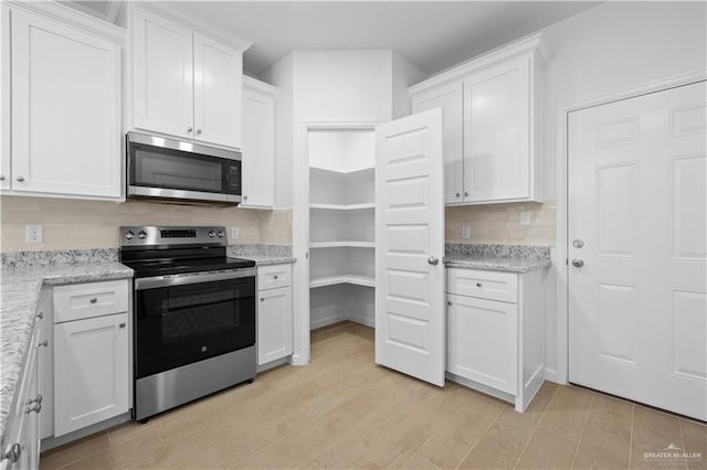 kitchen with light stone countertops, light wood finished floors, white cabinetry, and stainless steel appliances