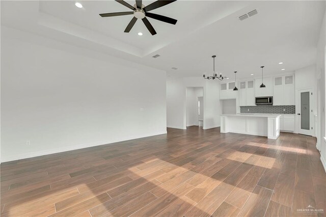 unfurnished living room featuring ceiling fan with notable chandelier, a raised ceiling, and dark wood-type flooring