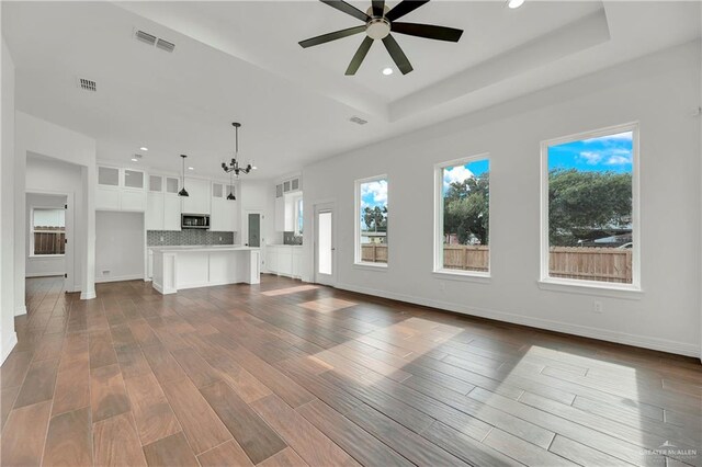 unfurnished living room featuring a raised ceiling, hardwood / wood-style floors, and ceiling fan with notable chandelier