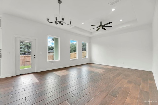 unfurnished room with ceiling fan with notable chandelier, a raised ceiling, and wood-type flooring