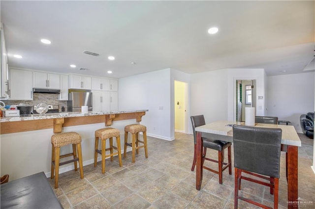 kitchen featuring light stone countertops, tasteful backsplash, a kitchen bar, white cabinetry, and appliances with stainless steel finishes