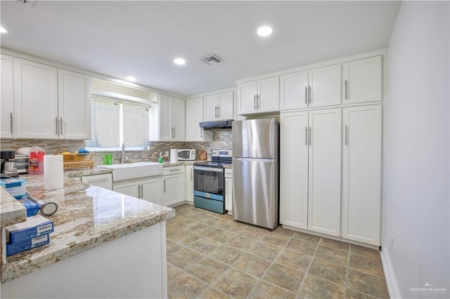 kitchen featuring light stone countertops, decorative backsplash, white cabinets, appliances with stainless steel finishes, and sink