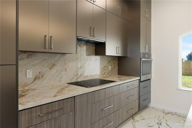 kitchen with gray cabinets, backsplash, black electric stovetop, light stone countertops, and stainless steel oven