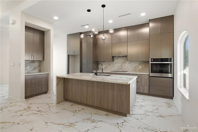 kitchen with an island with sink, sink, stainless steel oven, and decorative backsplash