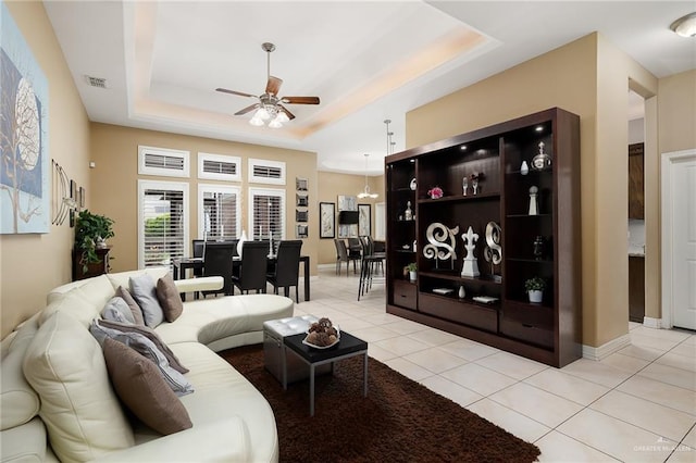 living room featuring a raised ceiling, ceiling fan, and light tile patterned flooring