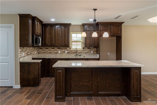 kitchen with sink, light stone countertops, decorative light fixtures, a kitchen island, and dark hardwood / wood-style flooring