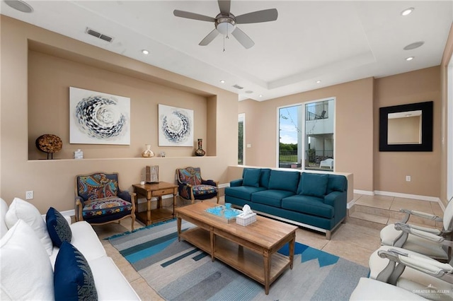 tiled living room with ceiling fan and a tray ceiling