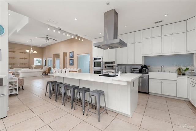 kitchen with island range hood, a kitchen island with sink, sink, white cabinetry, and a breakfast bar area