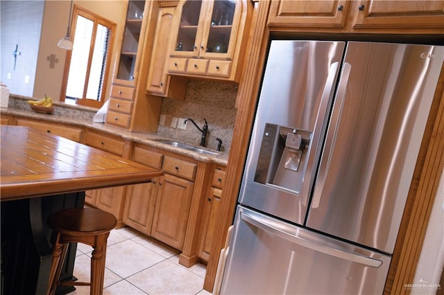 kitchen featuring light stone countertops, backsplash, sink, light tile patterned floors, and stainless steel fridge with ice dispenser