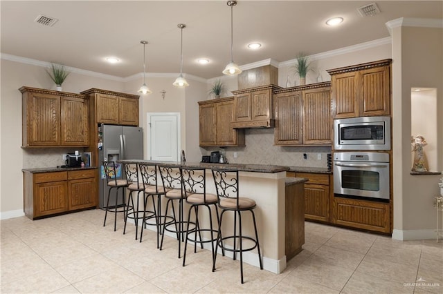 kitchen with a breakfast bar area, appliances with stainless steel finishes, ornamental molding, an island with sink, and decorative light fixtures