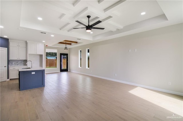 kitchen with coffered ceiling, a sink, white cabinets, open floor plan, and decorative backsplash